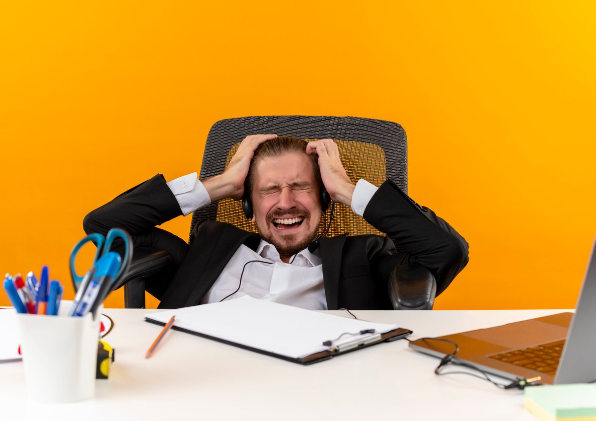 handsome-businessman-suit-headphones-with-microphone-going-wild-by-pulling-his-hair-sitting-table-offise-orange-background